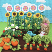 A crocheted garden featuring sunflowers, a squirrel, carrots, and tomatoes