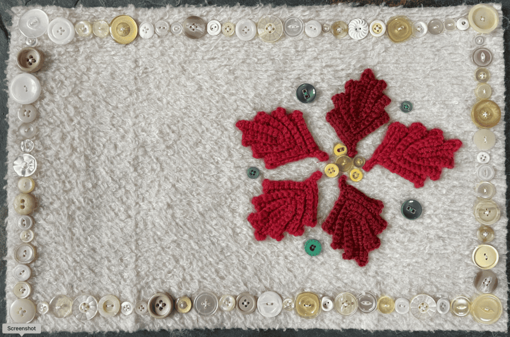 A fabric table mat with a crochet poinsettia on the right side, surrounded by decorations made of buttons 