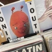 An orange crocheted toy is featured on one of the music album covers displayed at a bookstore.