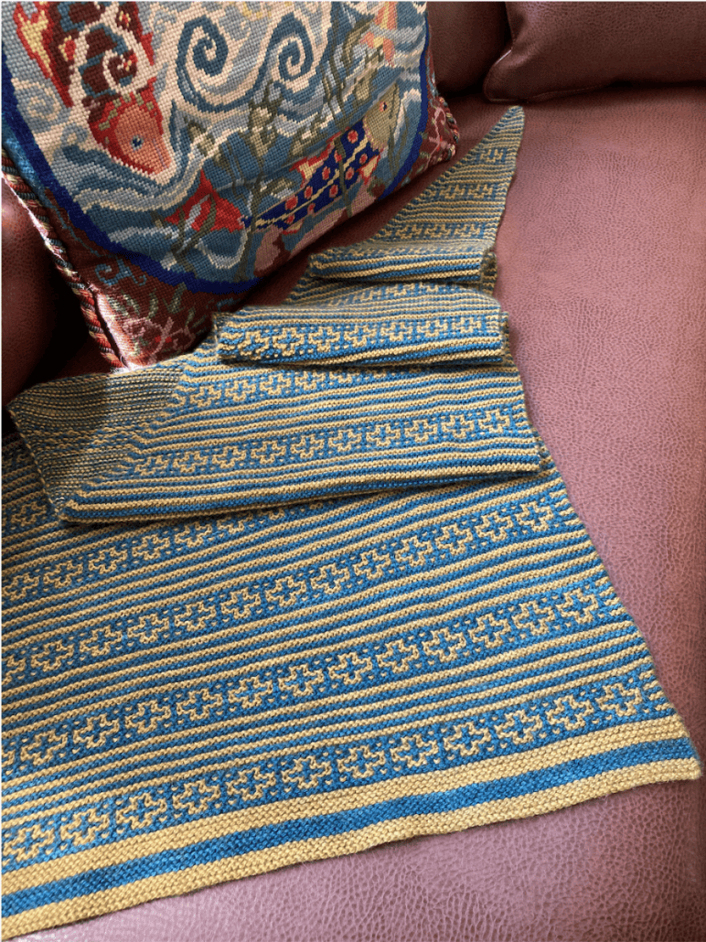 A knit yellow and teal shawl with alternating stripes and a cross pattern