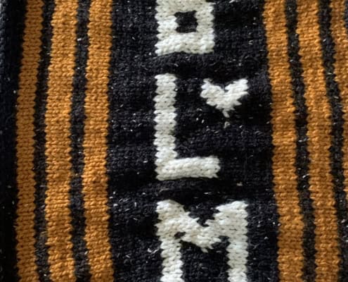 A black knitted banner with yellow stripes and the letters BLM knit in white