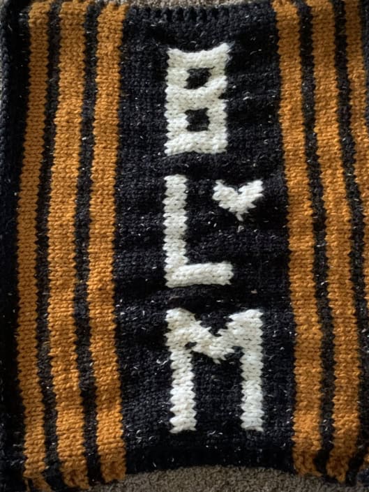 A black knitted banner with yellow stripes and the letters BLM knit in white