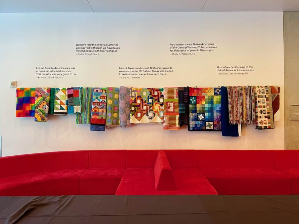 A display of handmade blankets against a white wall with text