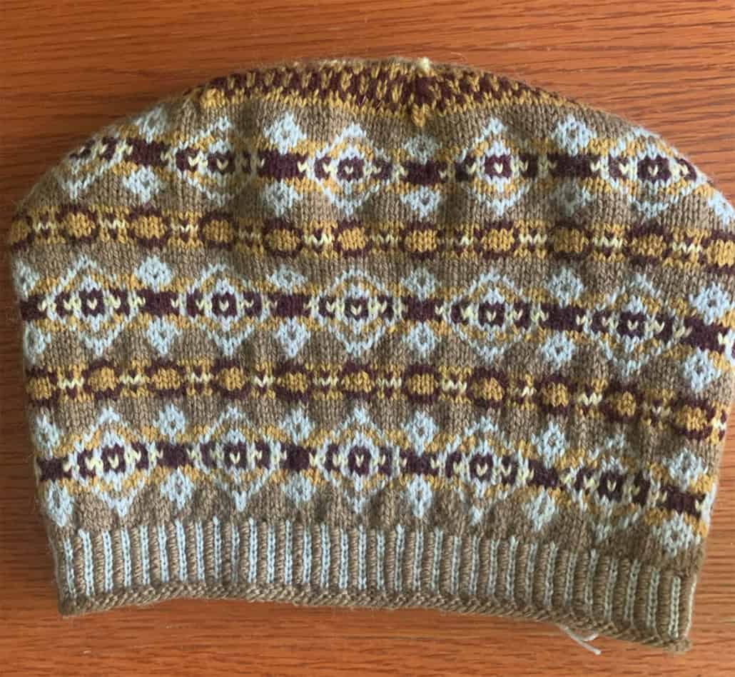 A stranded color-work hat, in the Fair Isle style, knitted in light brown, dark brown, gold, and white.