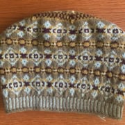 A stranded color-work hat, in the Fair Isle style, knitted in light brown, dark brown, gold, and white.