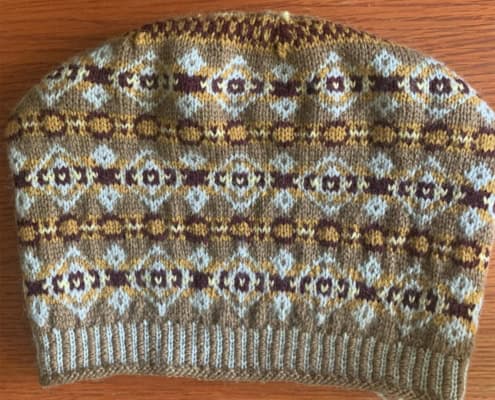 A stranded color-work hat, in the Fair Isle style, knitted in light brown, dark brown, gold, and white.